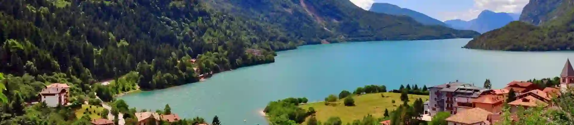 Molveno Lake in Italy, with colourful houses in the foreground and rolling hills alongside the lake