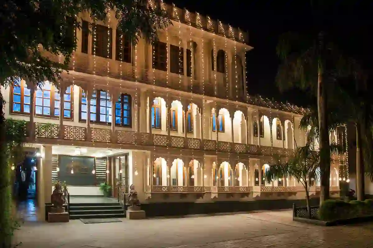 Grand exterior of the Ranthambore Bagh Palace hotel at night, with it's intricately designed façade lit by warm string lights
