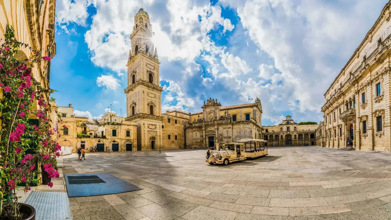 A square in Lecce, Puglia, Italy, featuring a historic tower and a land train for tourists