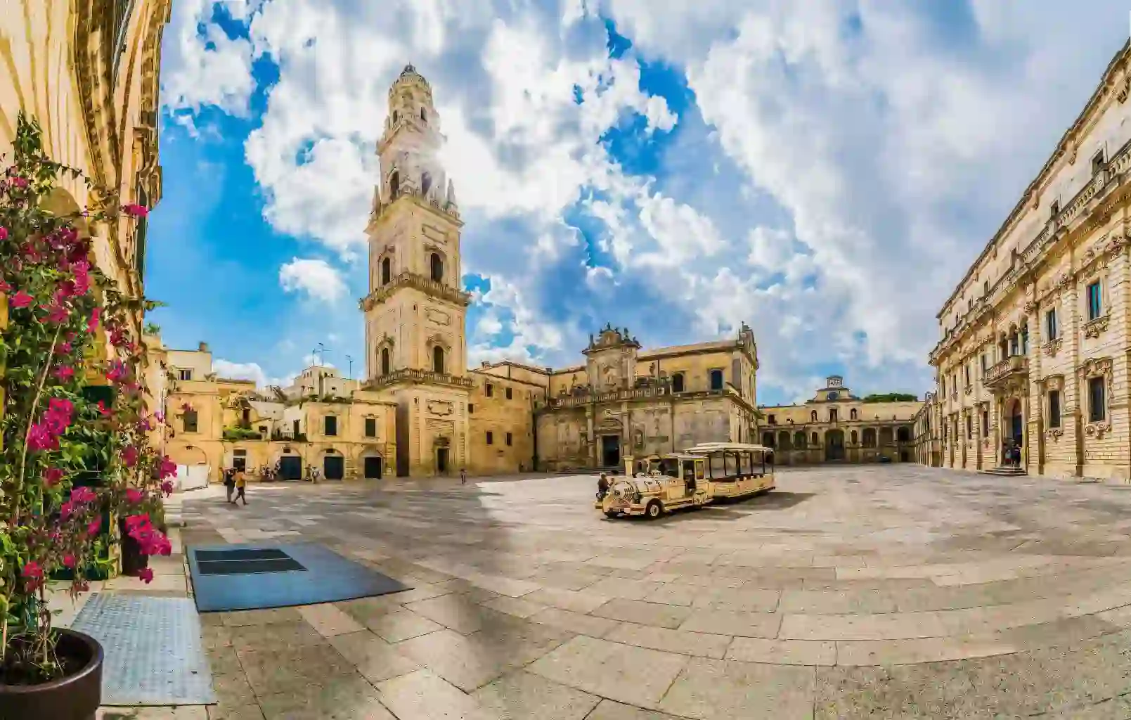 A square in Lecce, Puglia, Italy, featuring a historic tower and a land train for tourists