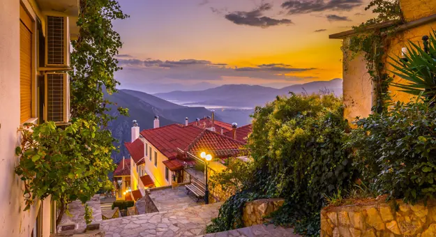 View from Delphi in the mountains, looking out on the landscape with sunset and silhouette of mountains. Steps and buildings in the forefront