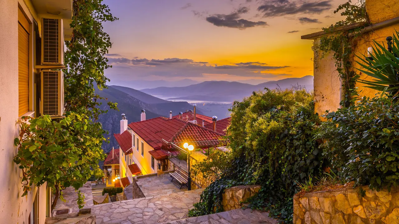 View from Delphi in the mountains, looking out on the landscape with sunset and silhouette of mountains. Steps and buildings in the forefront