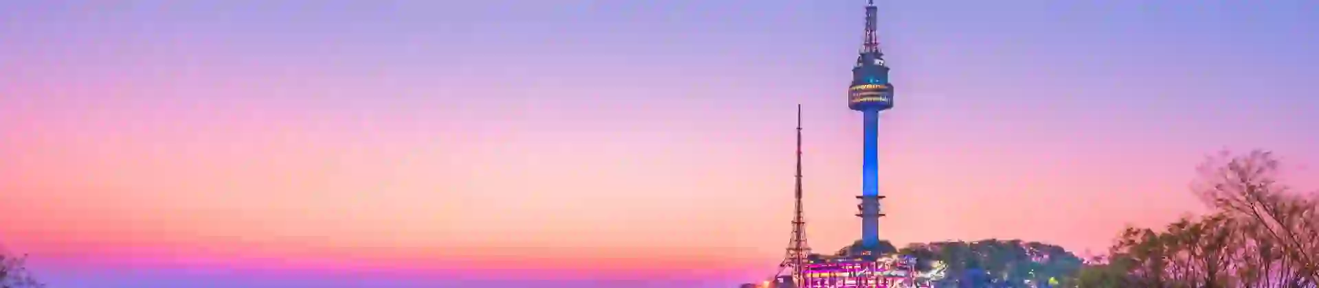 A view of Seoul Tower in South Korea at sunset, with warm orange and pink hues lighting up the sky and the cityscape below