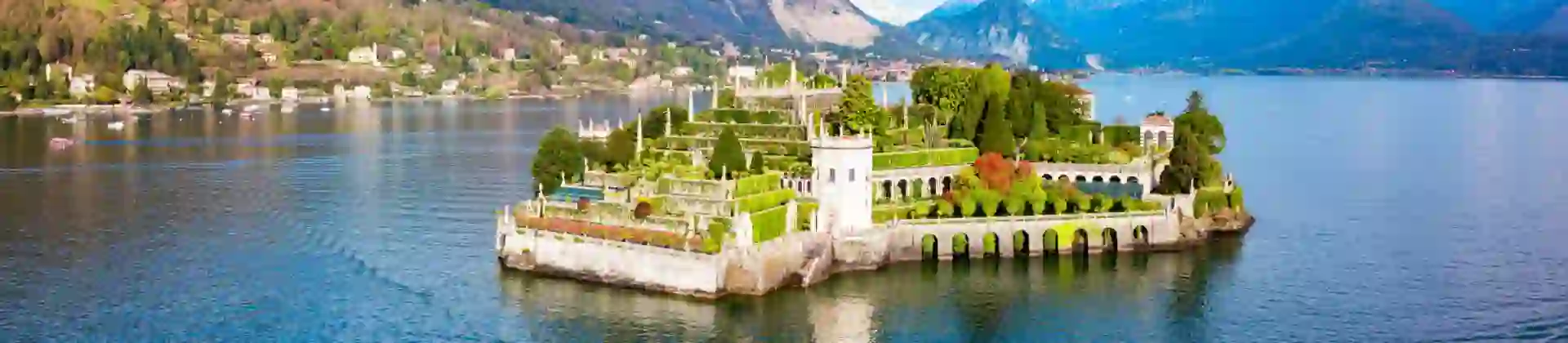 A picturesque view of Isola Bella on Lake Maggiore in Italy, featuring its ornate terraced gardens, elegant architecture and the surrounding mountains reflected in the water