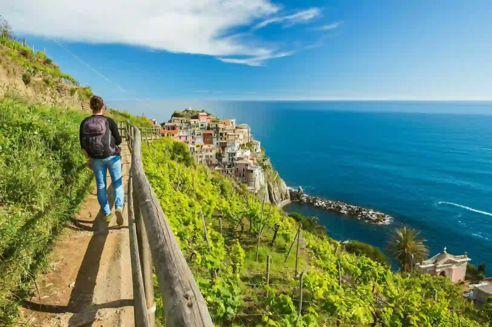 A person walking along a cliffside path in Cinque Terre, overlooking colourful buildings and the blue sea
