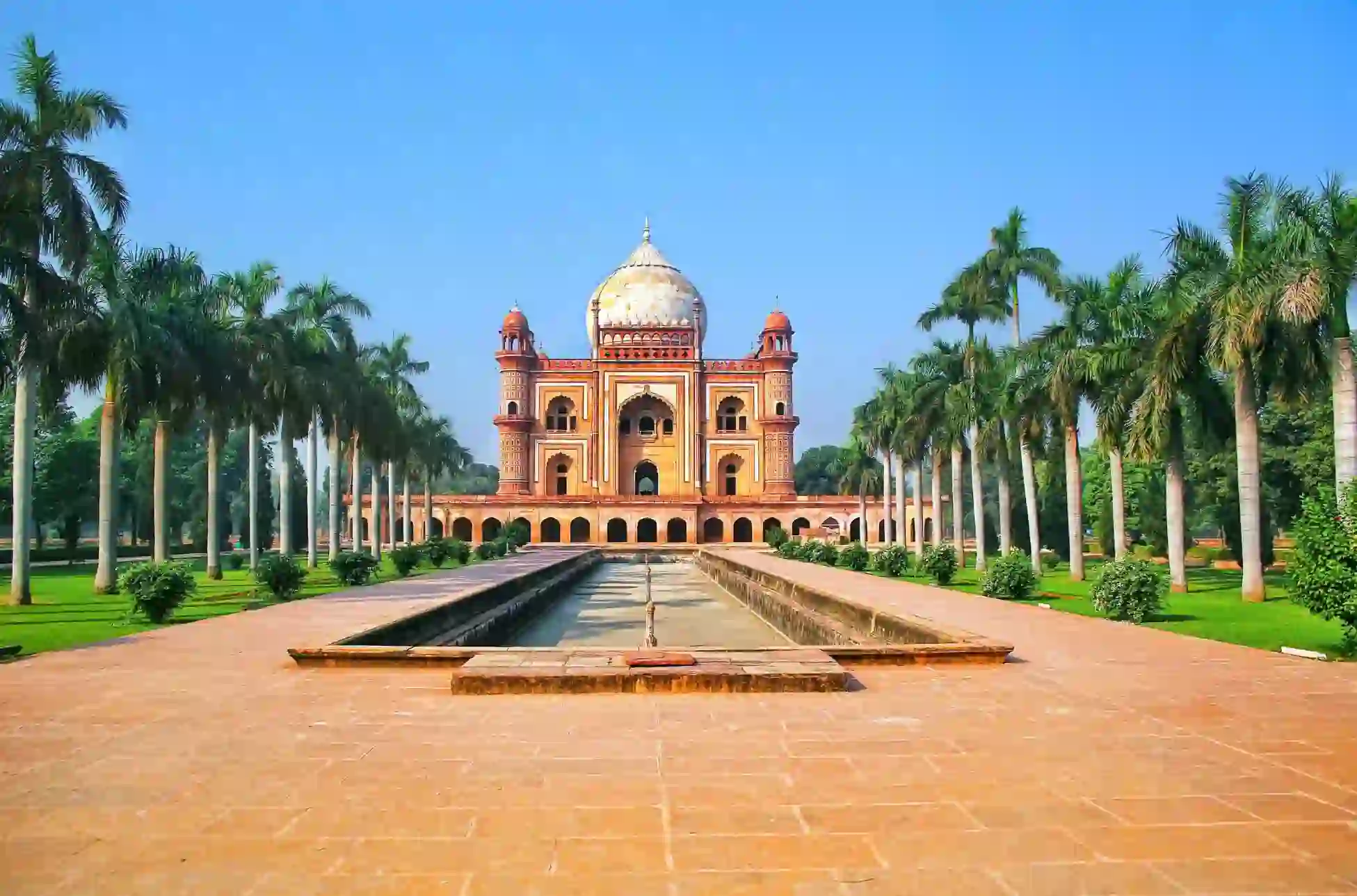 Front view of Humayun's Tomb in Delhi, India, framed by symmetrical rows of palm trees and a long reflecting pool under a clear blue sky