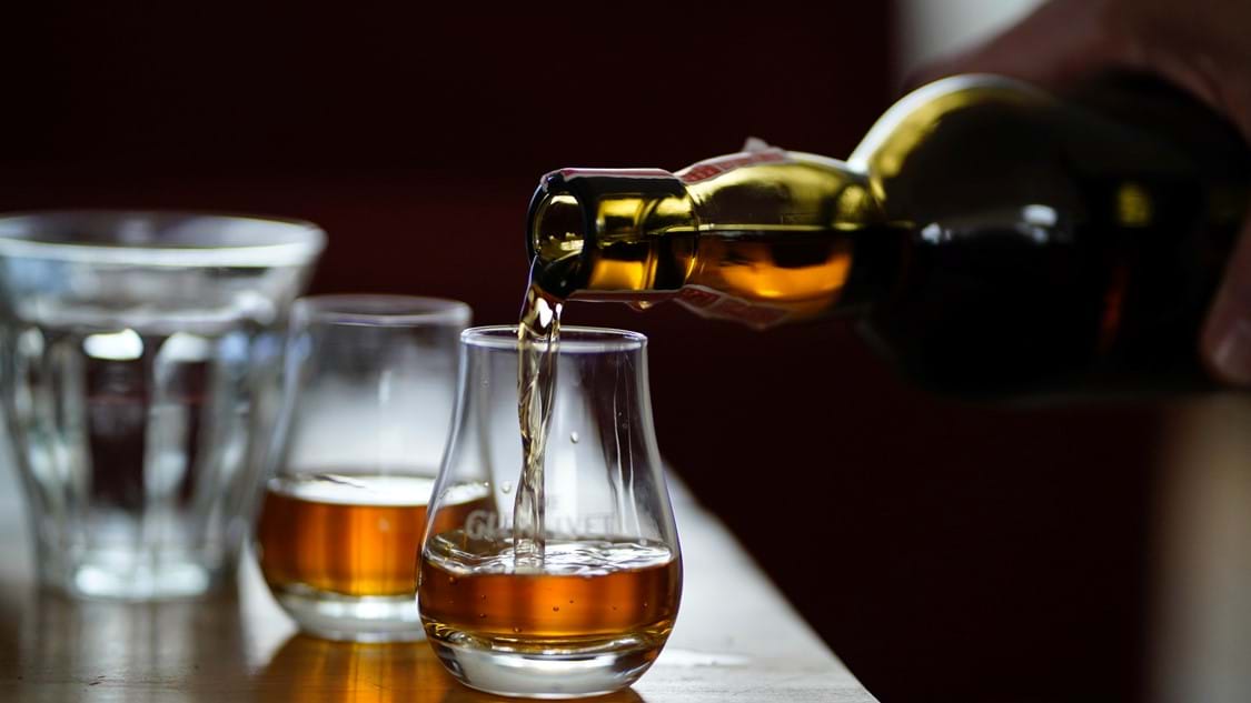 Close up of a glass of Scottish whisky being poured with dark lighting