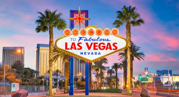 "Welcome to Fabulous Las Vegas, Nevada” sign at dusk, with palm trees and city lights in the background